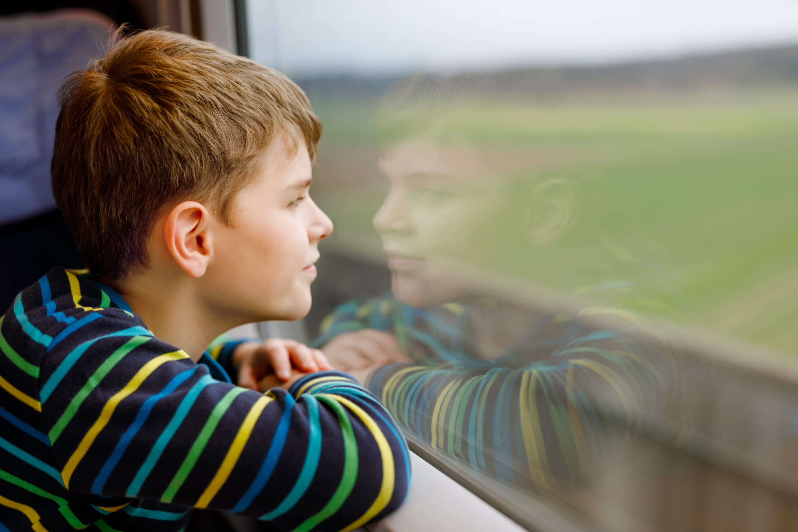 adorable kid boy traveling by train. happy smiling child looking out of the window during train moving. kid dreaming and wondering. family vacations and journey trip.